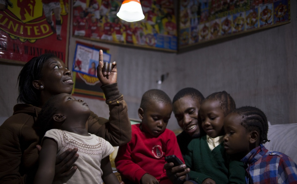 На фото: семья из Африки в освещенном помещении. Приобрести свет стало возможно благодаря социальной компании D.light, которая существует благодаря импакт-инвестициям. Изображение с сайта cleantechnica.com